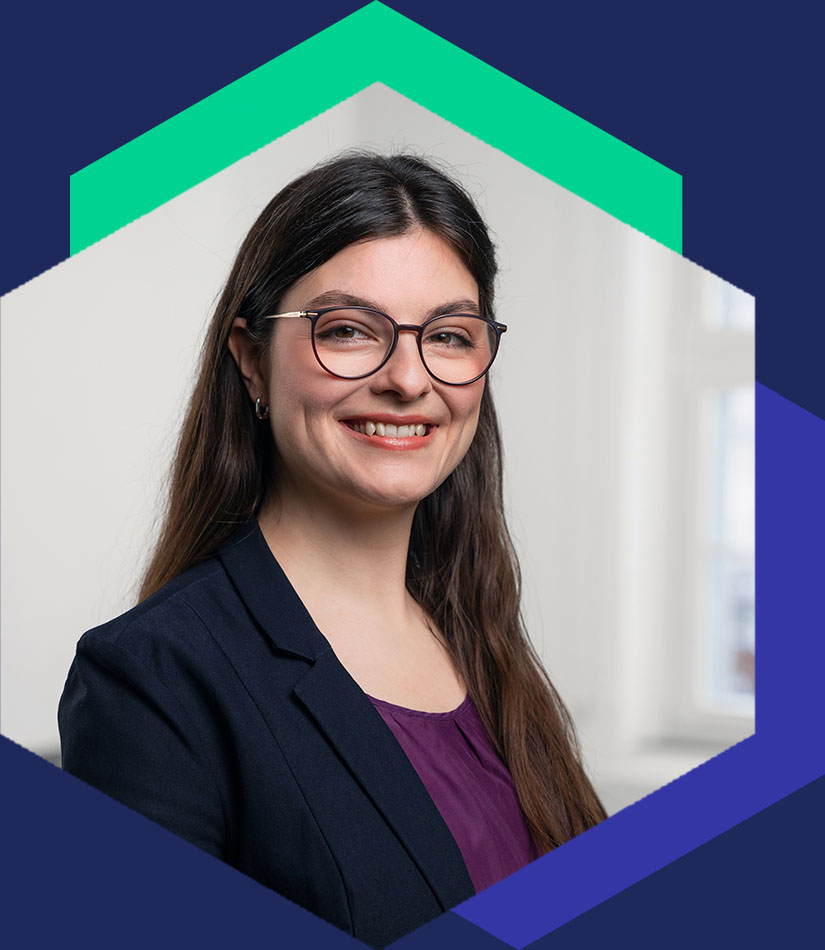 Porträt von Adriane Klaus mit Brille, dunklem Blazer und lila Oberteil, grafisch eingefasst in einem modernen Hexagon-Design, Beraterin für PR und strategische Kommunikation bei WeichertMehner