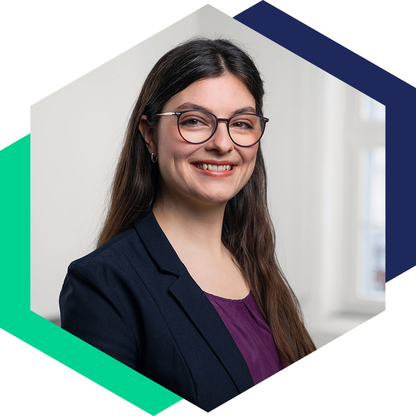 Porträt von Adriane Klaus mit Brille, dunklem Blazer und lila Oberteil, grafisch eingefasst in einem modernen Hexagon-Design, Beraterin für PR und strategische Kommunikation bei WeichertMehner