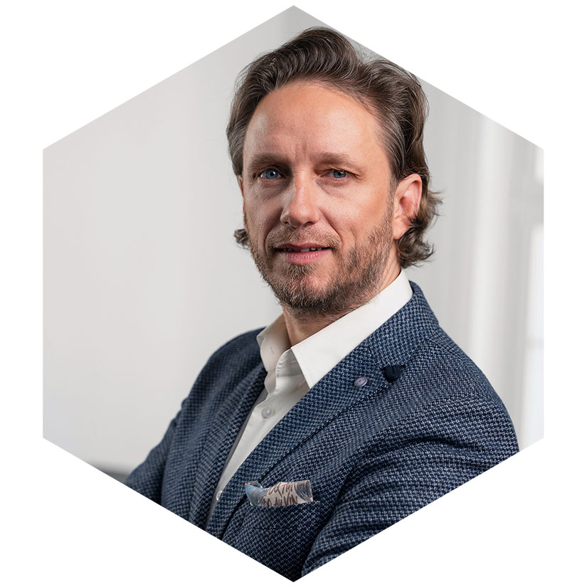 Dr. Erik Fritzsche im blauen Sakko mit Einstecktuch, grafisch eingerahmt in einem Hexagon-Design, Senior Berater für strategische Kommunikation und Krisenmanagement bei WeichertMehner