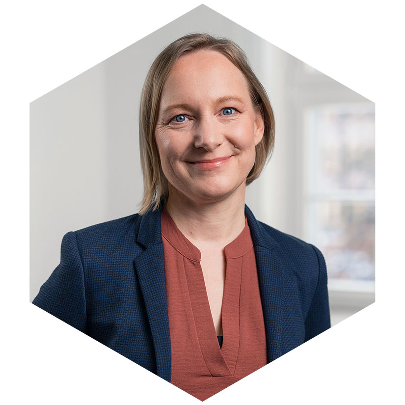 Porträt von Steffi Petersen im dunkelblauen Blazer und rostbraunem Oberteil, eingefasst in das hexagonale Corporate-Design-Element, Art Director bei WeichertMehner